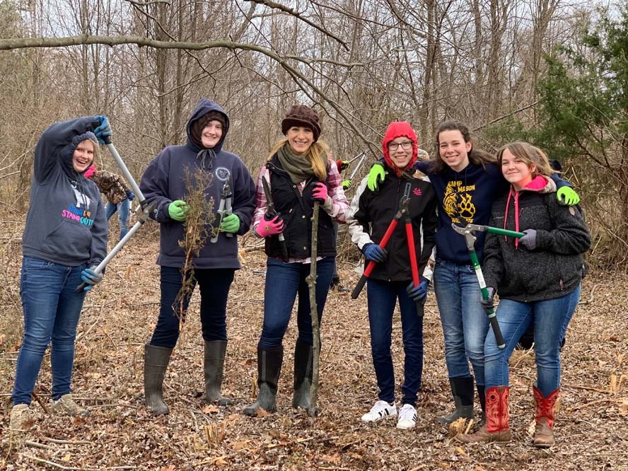 Group-shot of women in woods holding sticks and branch cutters