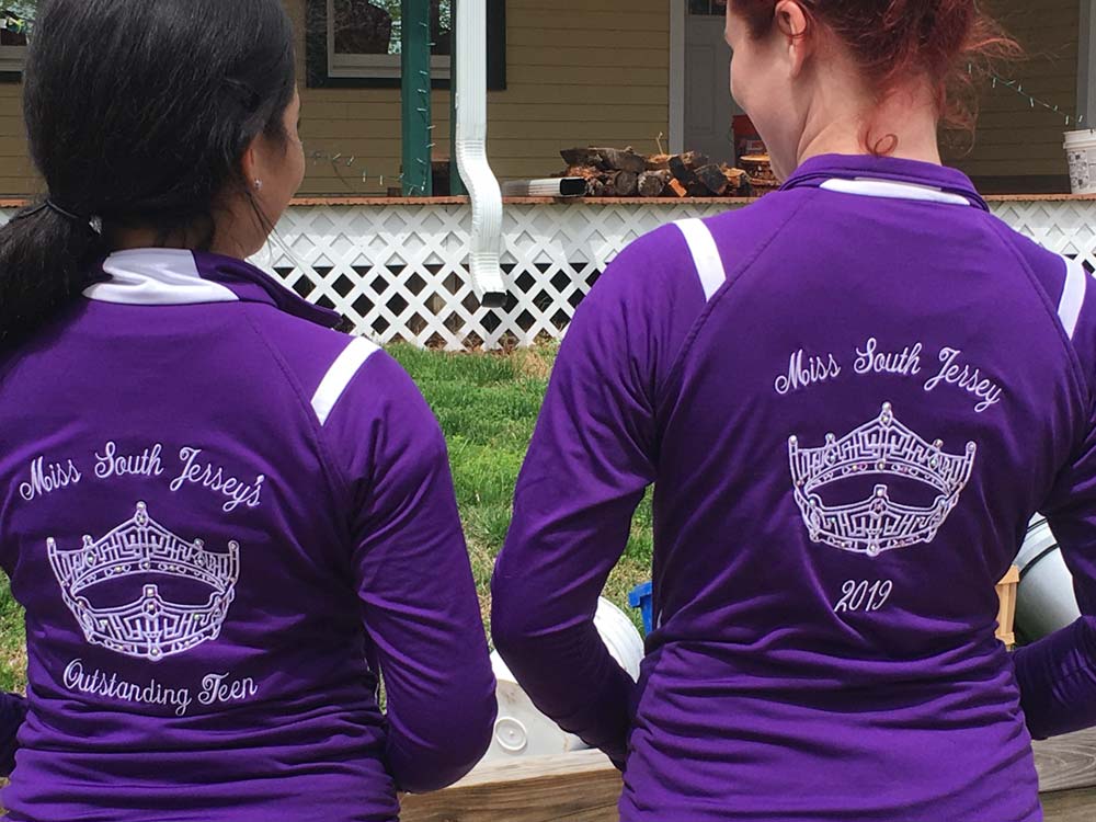 Close up of backs of 2 girls in purple jumpsuit jackets standing infront of building