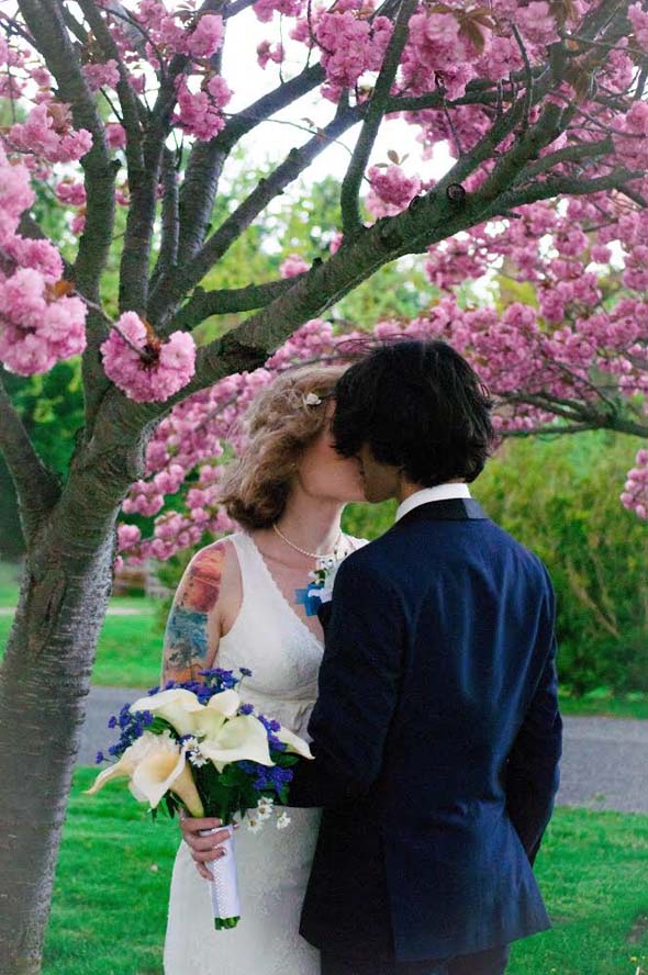 Bride and groom kissing under tree with pink flowers