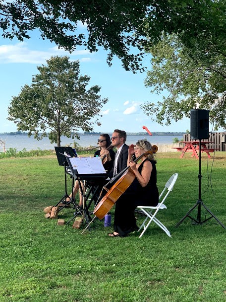 Woman holding cello with two other musicians next to her outside under tree