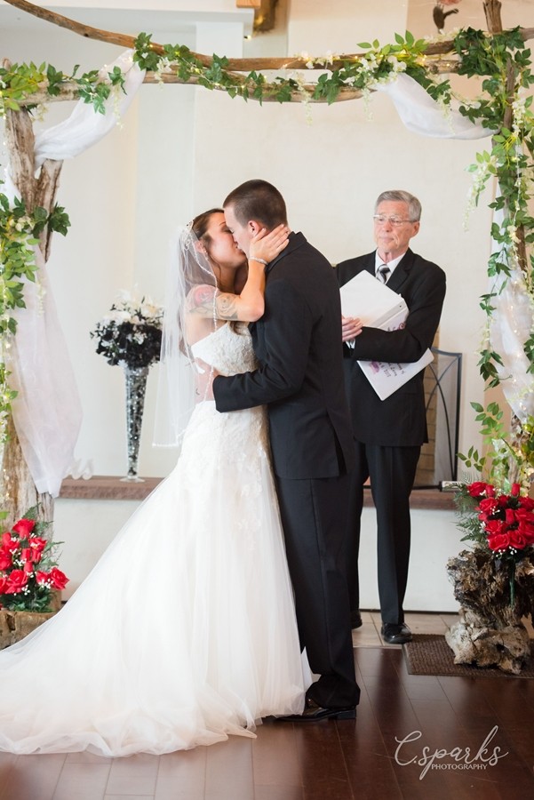 Bride and groom kissing under manor, priest behind them