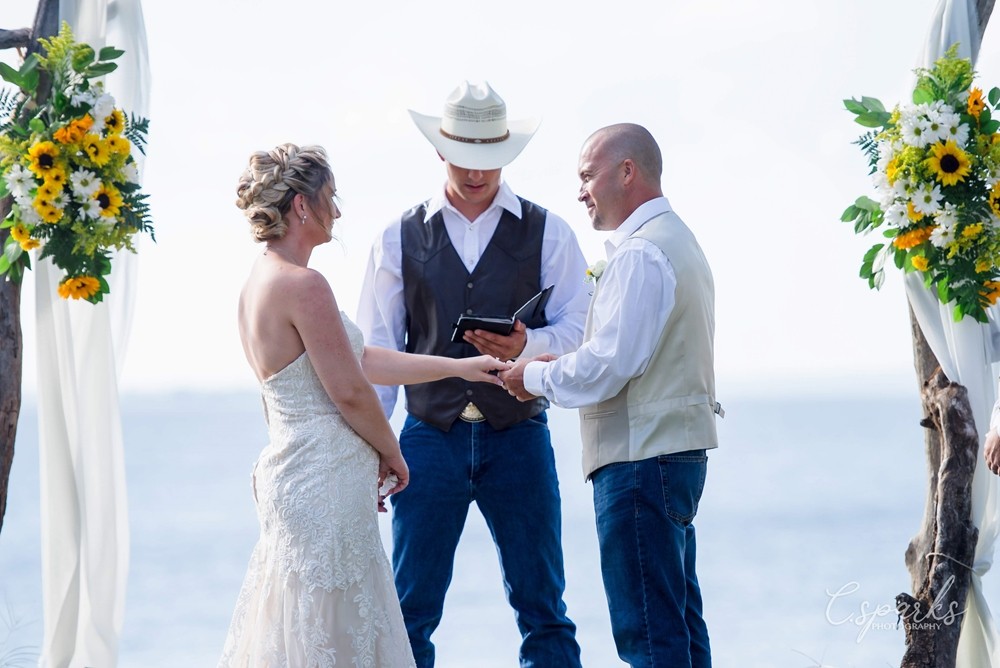 Bride and groom holding hands under manor, priest wearing cowboy hat