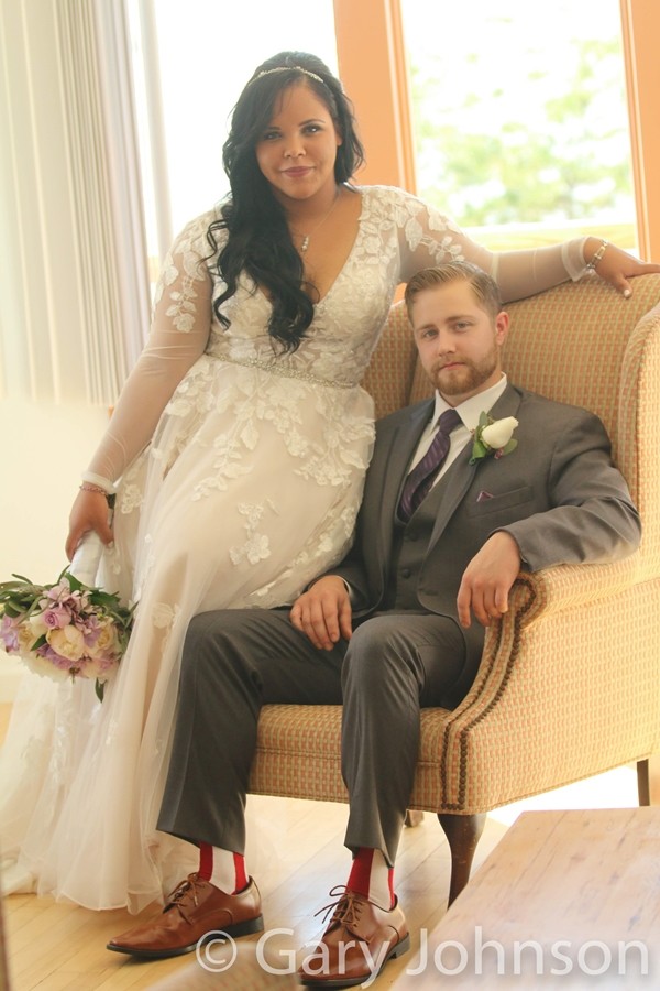 Groom sitting in char with bride leaning on side of chair