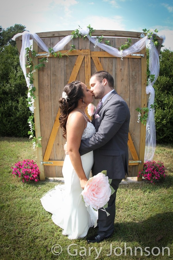 Bride and groom kissing in front of wooden backdrop in daylight