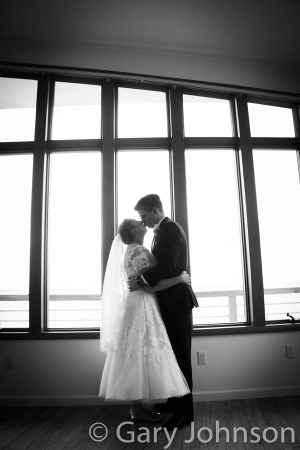 Black and white photo of bride and groom kissing infront of windows