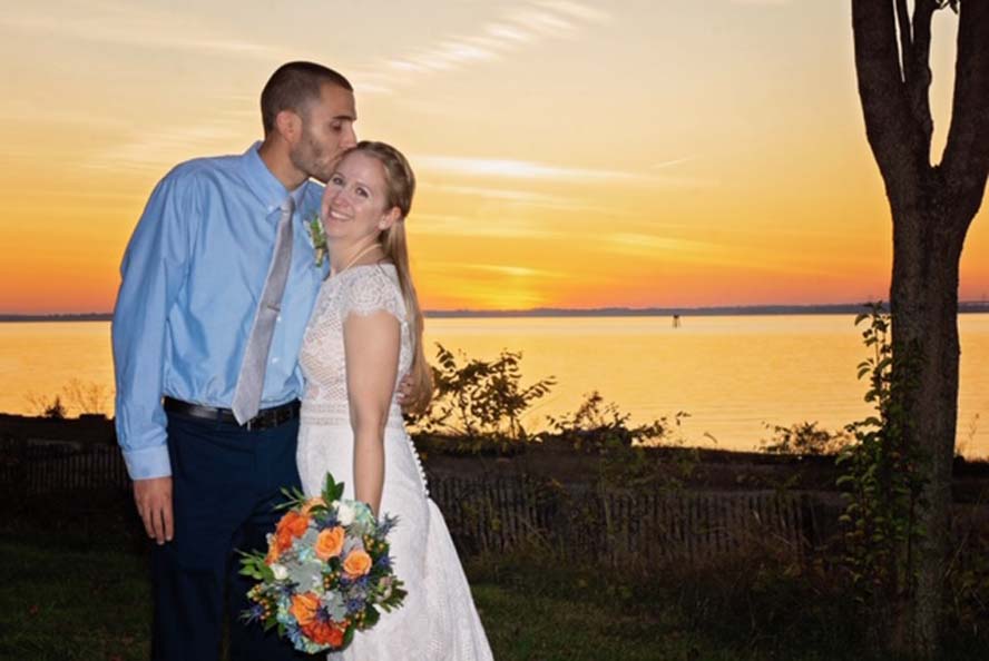 Groom kissing bride's forehead infront of sunset