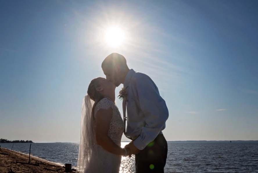 Bride and groom kissing infront of sun